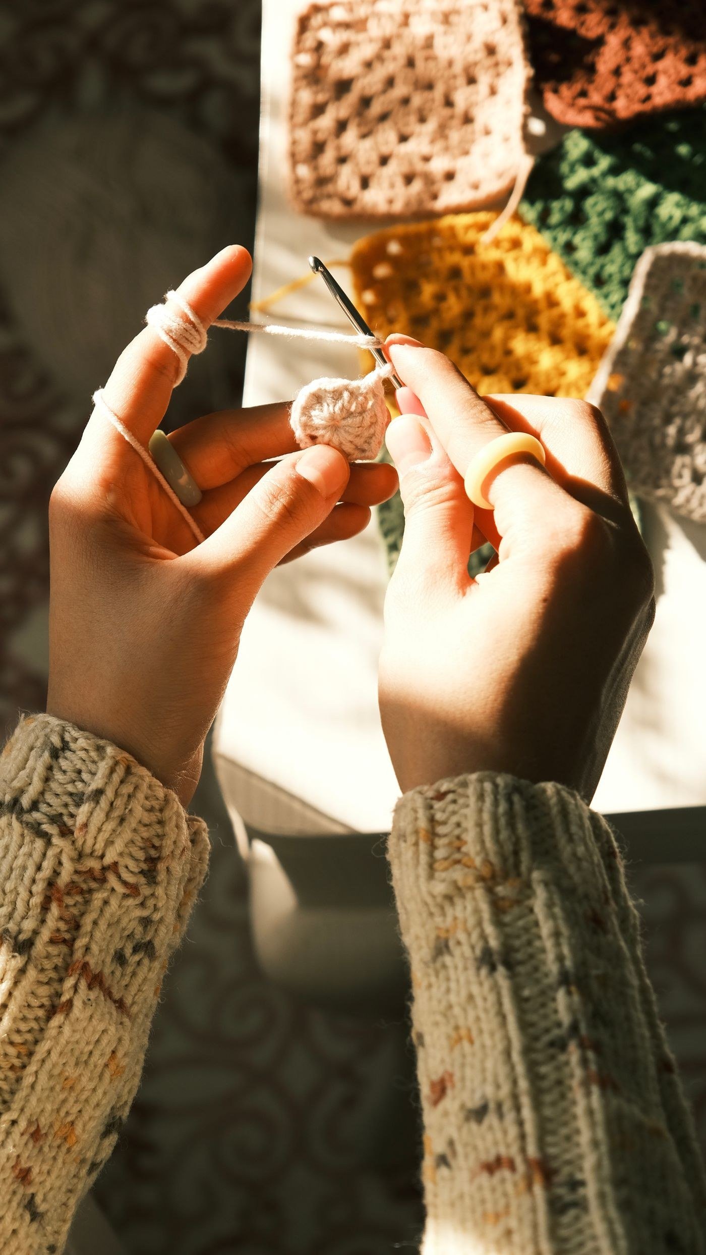Hands crocheting colorful granny squares in warm light