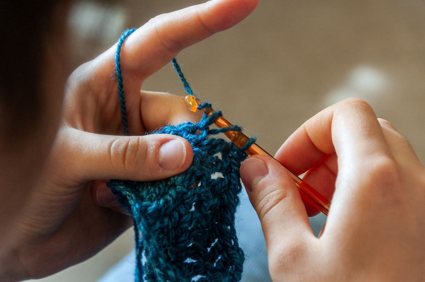 Hands crocheting a blue yarn piece with a hook