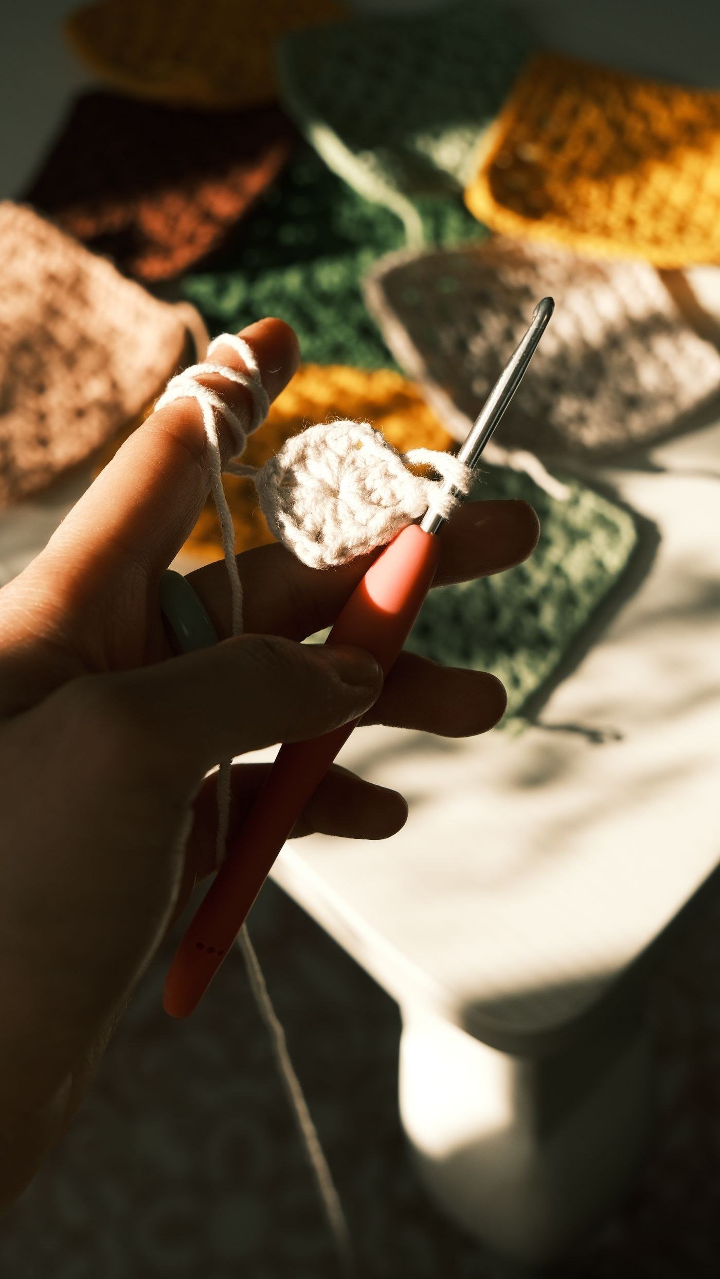 A hand holding a crochet hook working granny squares